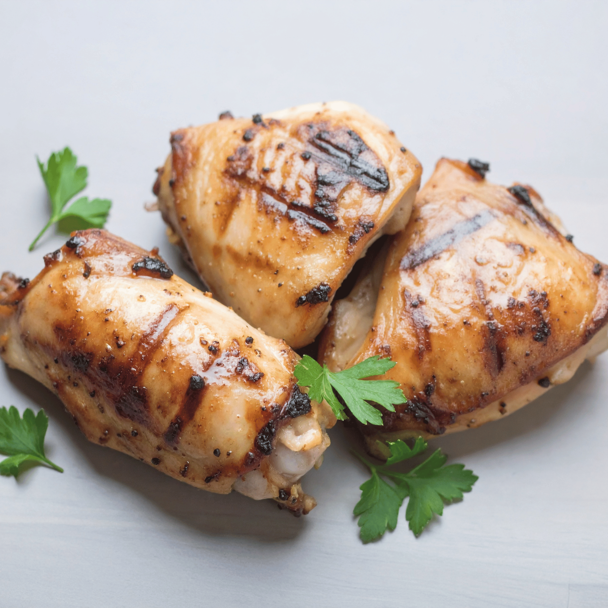 Grilled chicken thighs with parsley on a light gray background