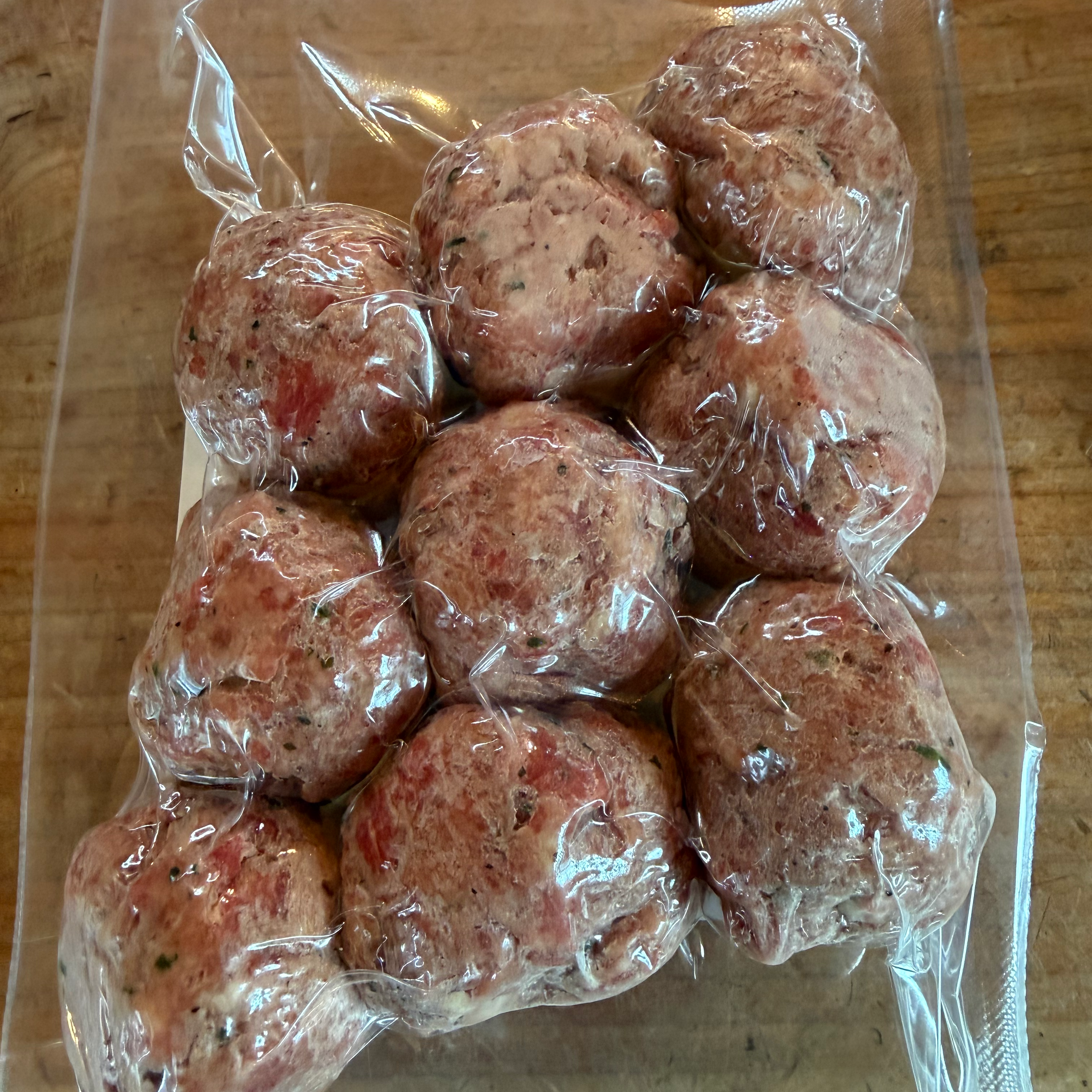 Packaged meatballs in clear plastic on a wooden surface