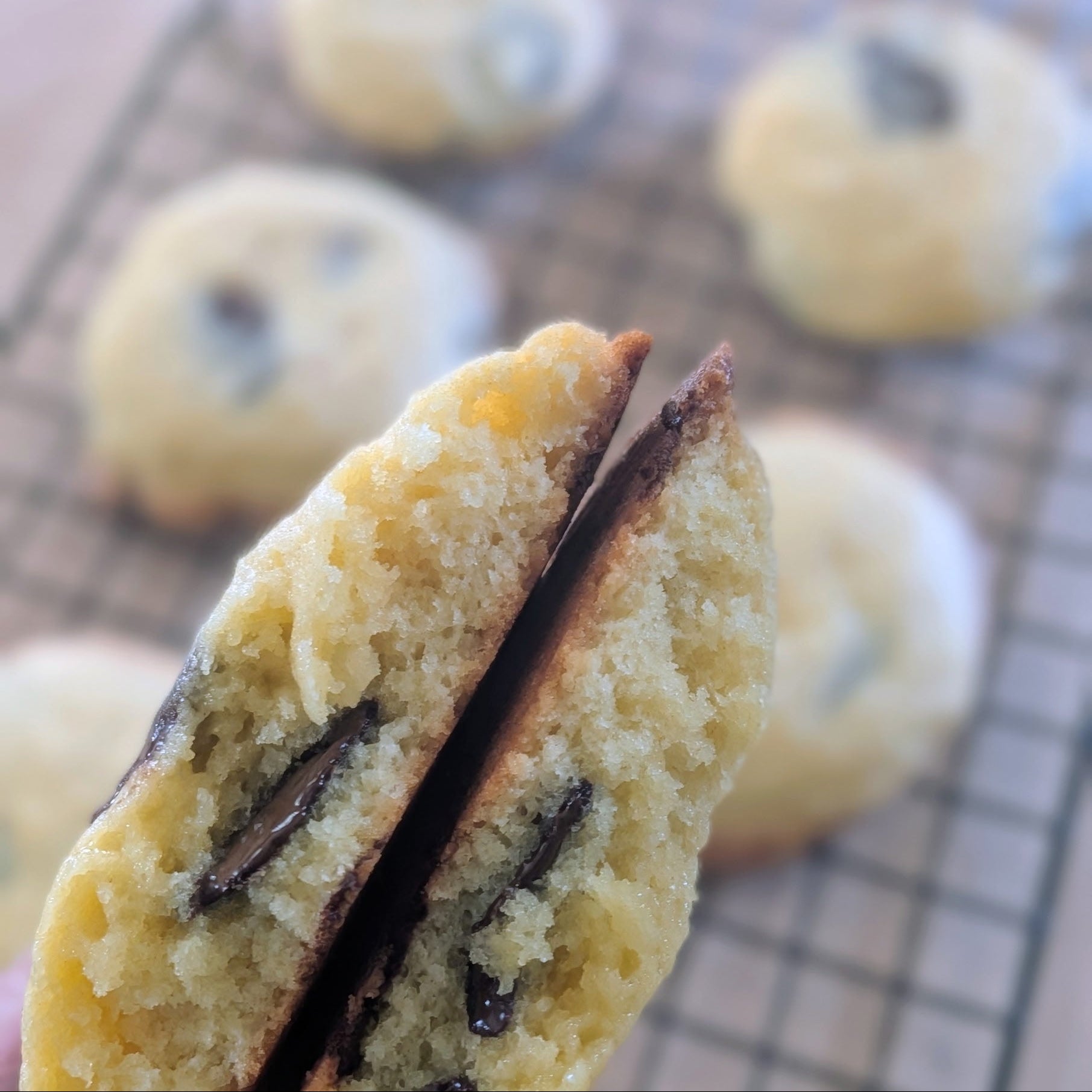Close-up of a cookie with chocolate filling, with more cookies on a cooling rack in the background.