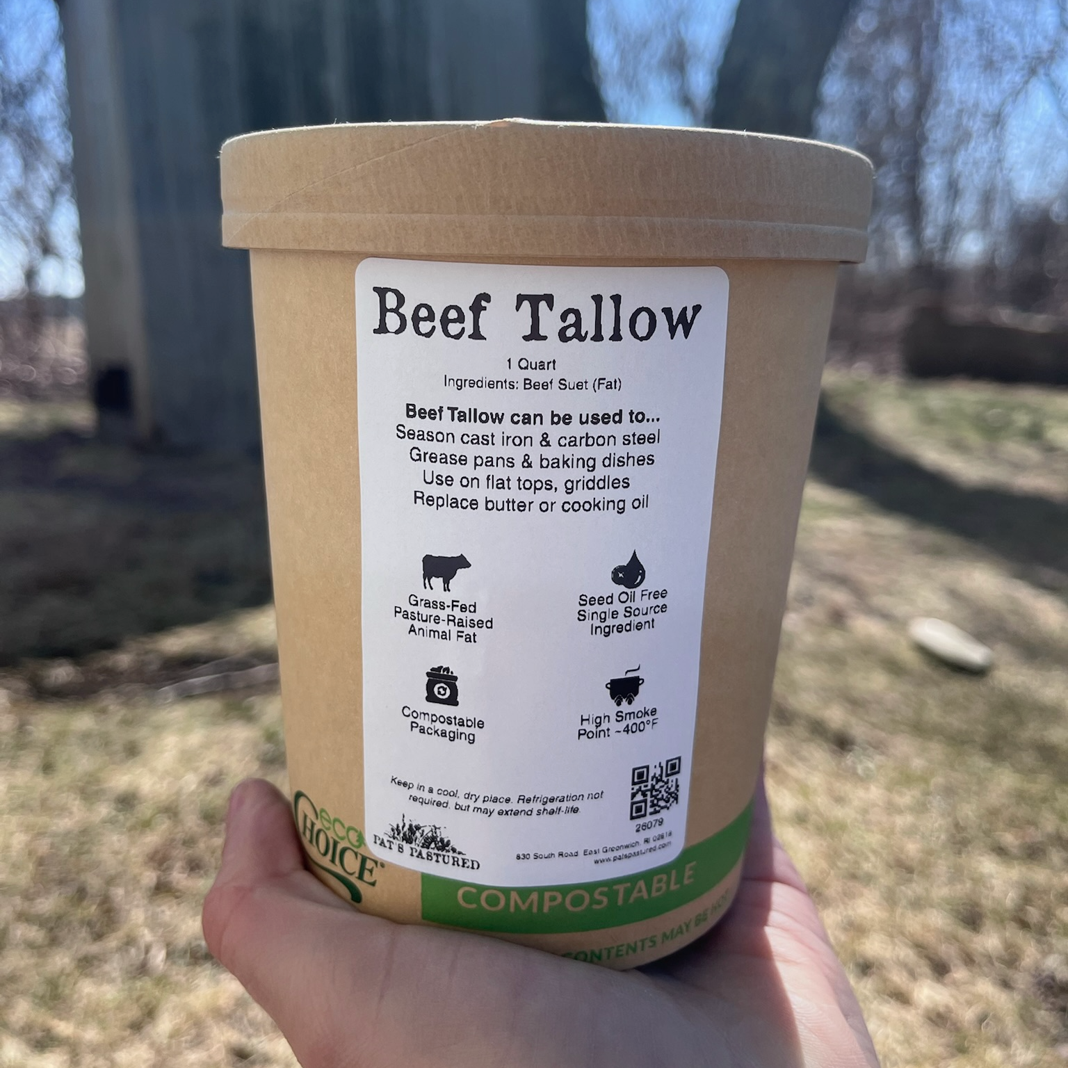 Hand holding a container of beef tallow with a label, outdoors.